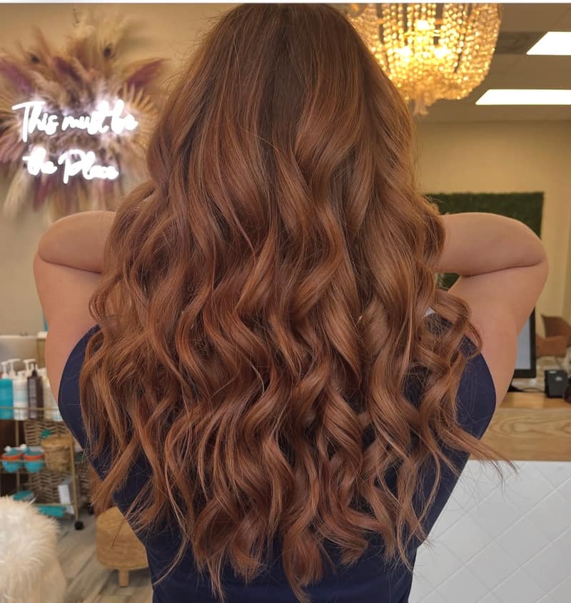 Copper-brown beach waves under the salon chandelier